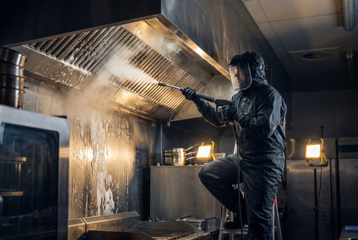 Technician steam-cleaning a commercial kitchen exhaust hood at night in Carrollton, TX